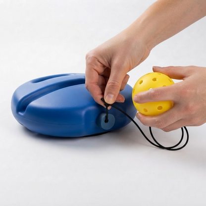 Hands pressing the elastic cord of a replacement pickleball into the anchor collar on the PickleBall Pro base