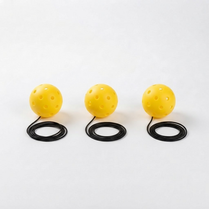Three optic yellow 40-hole PickleBall Pro replacement pickleballs, each with a coiled black elastic cord, on a white studio background